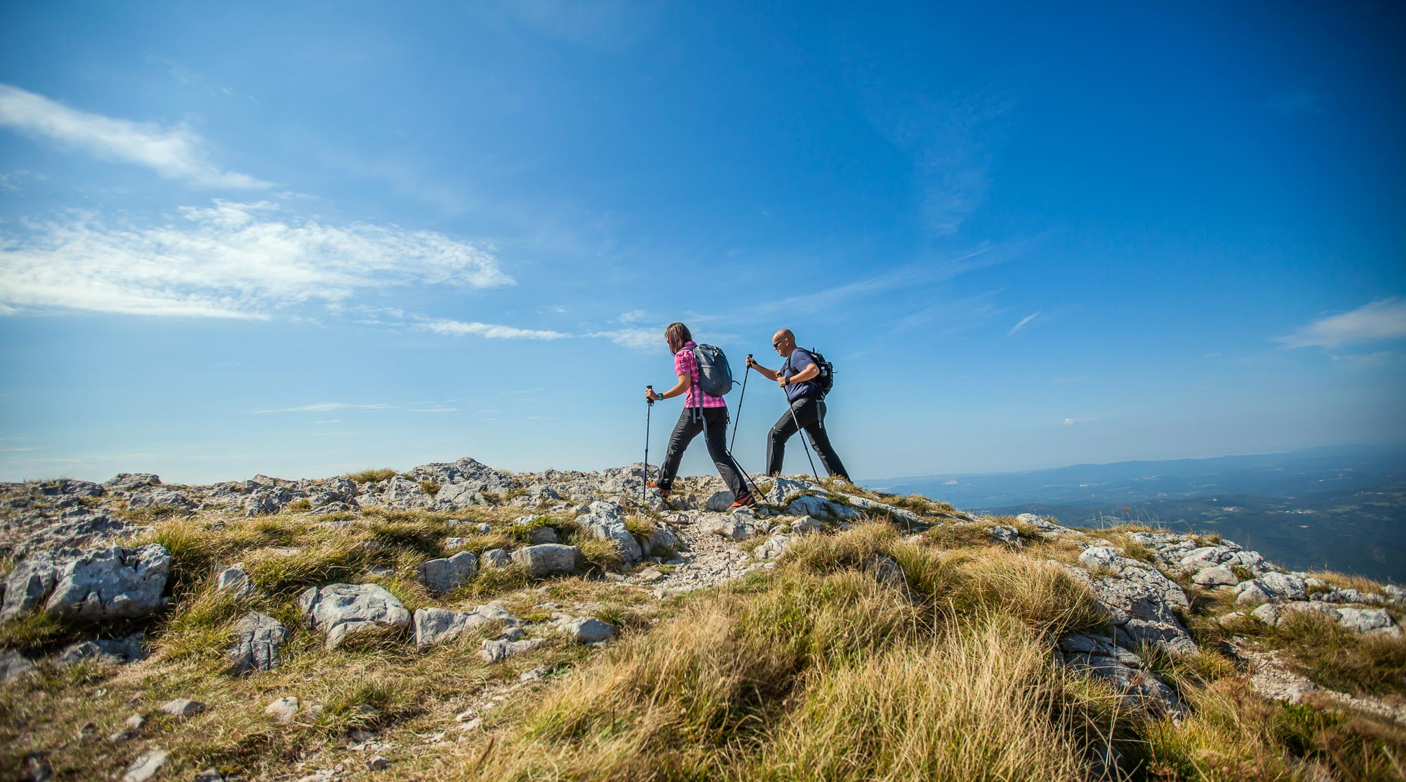 A couple hiking on Nanos Plateau in Slovenia against a blue sky